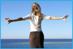 Online Mall image of a woman taken from behind her with her arms streached out wide like a bird as she faces the wind looking over a see view.